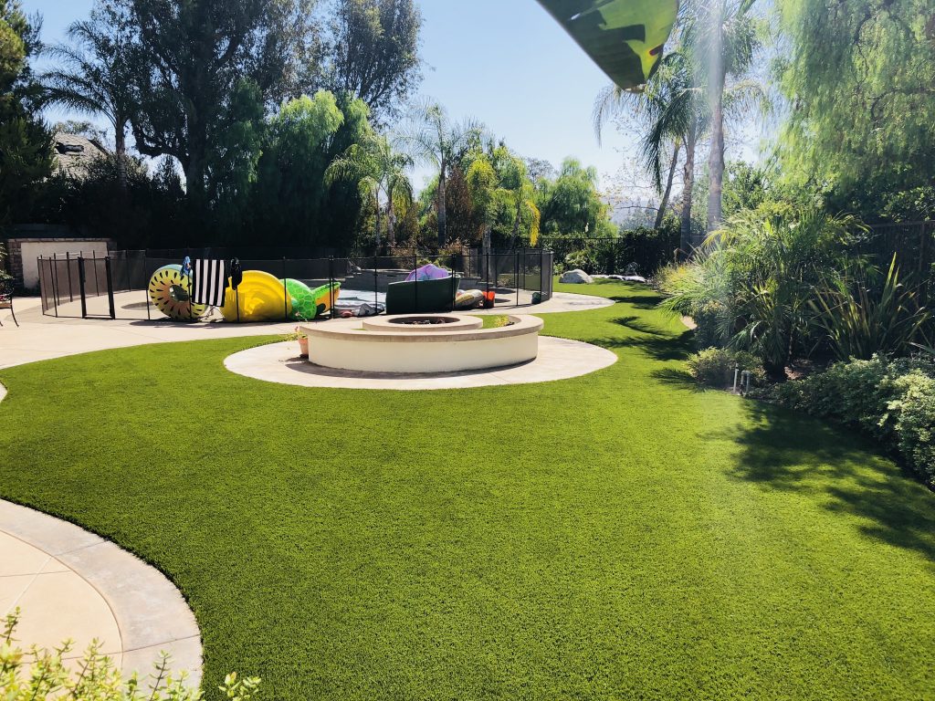 Custom artificial turf backyard installation with firepit and playset by Green Forever Turf Texas